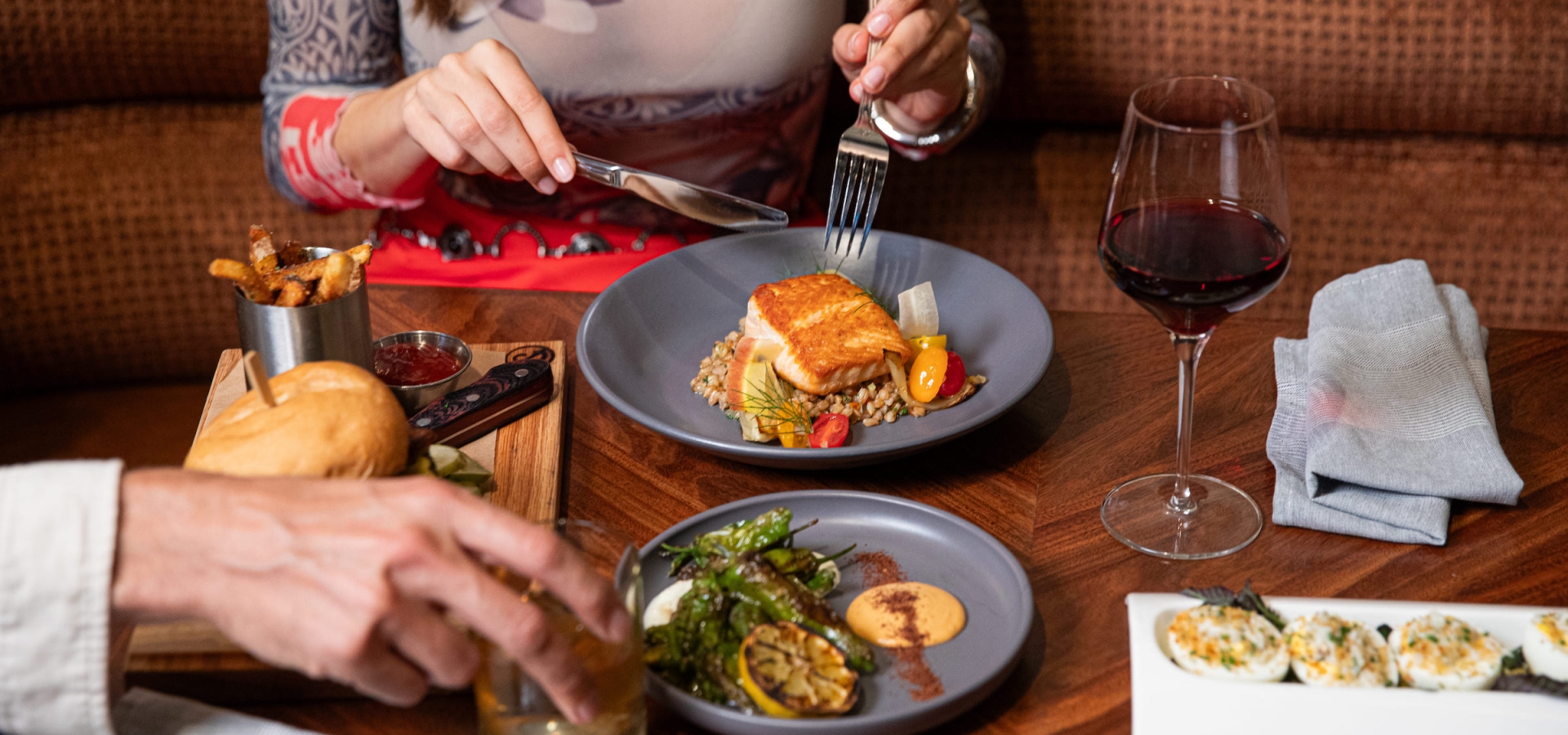A couple sharing a variety of dishes from seared fish on farro, devilled eggs and a burger and fires