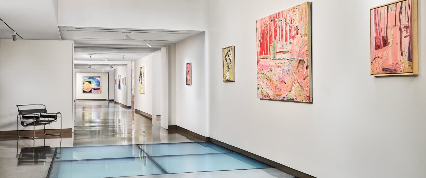 An art gallery hallway displays various colorful abstract paintings on white walls, featuring a light blue glass floor and a dark beamed ceiling.