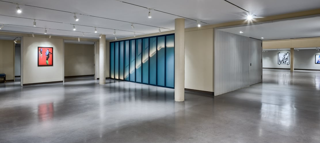 A long, blue-framed glass wall displays an illuminated diagonal pattern within a brightly lit modern interior space with a polished concrete floor.