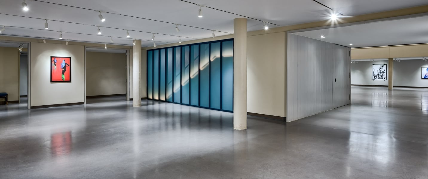 A long, blue-framed glass wall displays an illuminated diagonal pattern within a brightly lit modern interior space with a polished concrete floor.