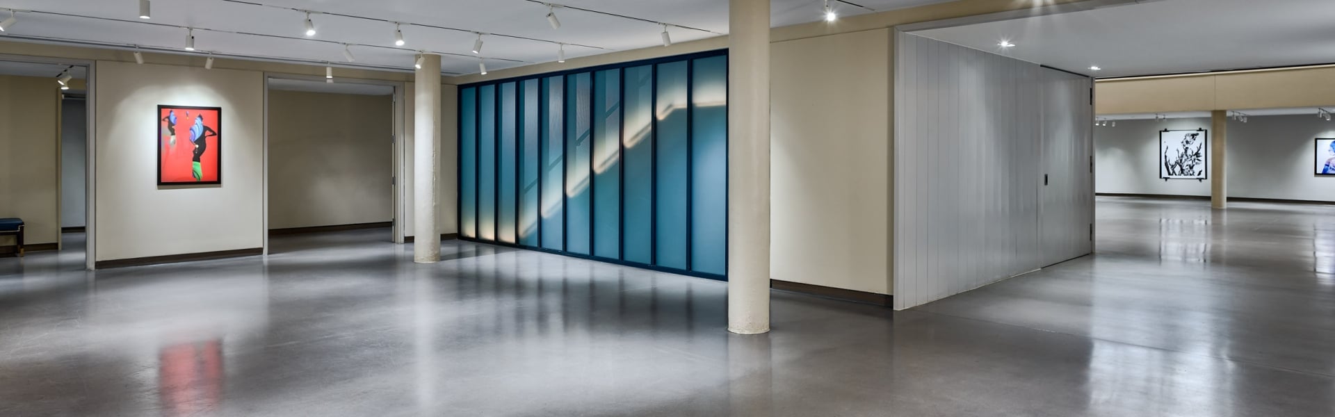A long, blue-framed glass wall displays an illuminated diagonal pattern within a brightly lit modern interior space with a polished concrete floor.