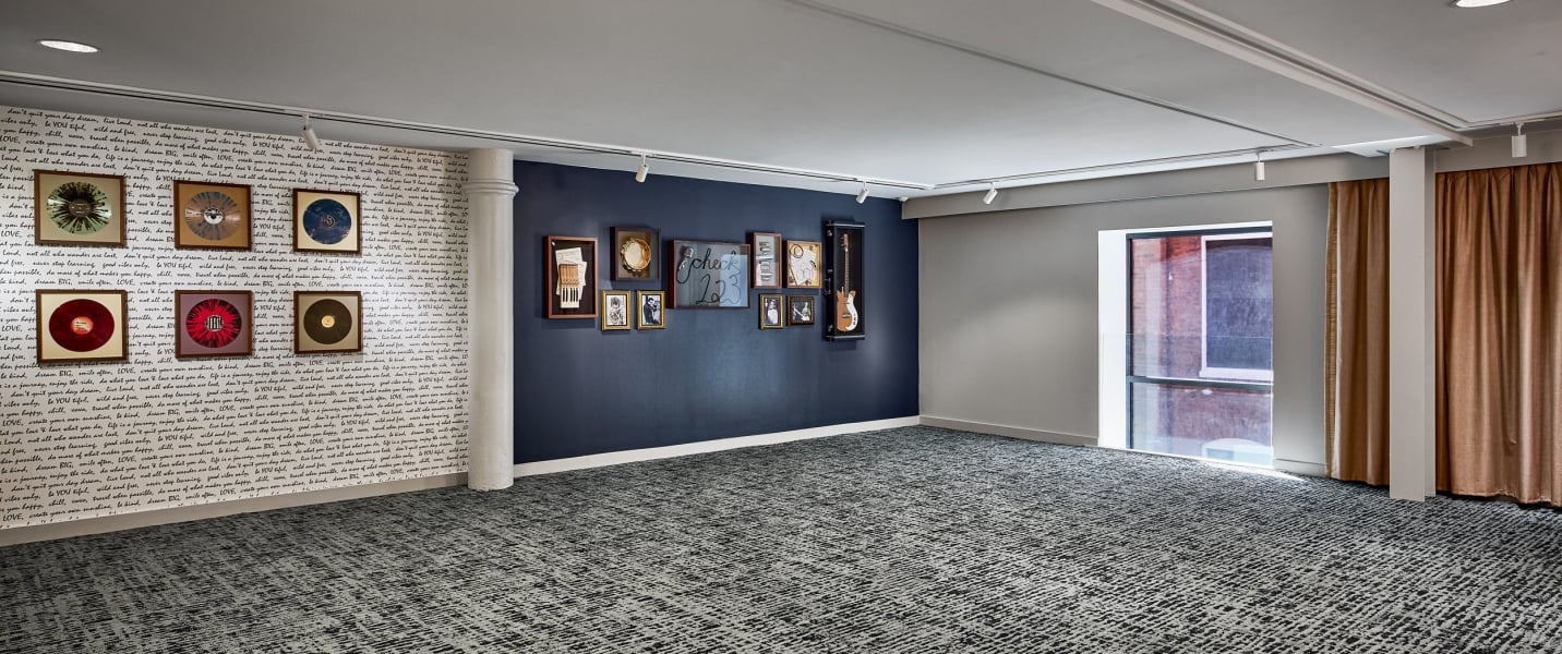 Room walls feature framed vinyl records and various artworks, including 'check 123' and a guitar, in a space with patterned carpet, a large window, and brown curtains.