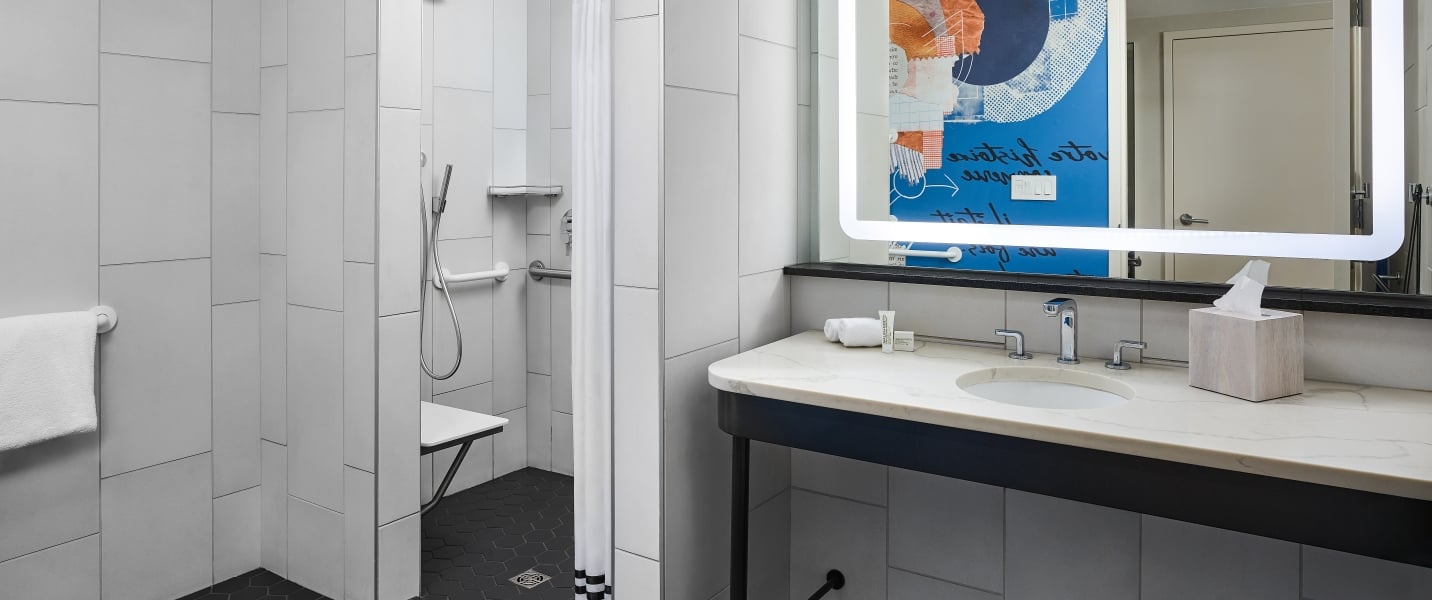 A bathroom with an accessible shower stall, with seat and shower wand, in a suite at the Untitled Nashville