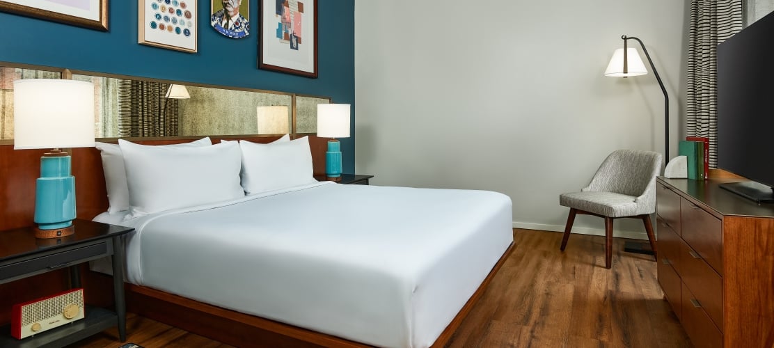 A large bed next to accent accent wall with art in a spacious guestroom at the Untitled Nashville