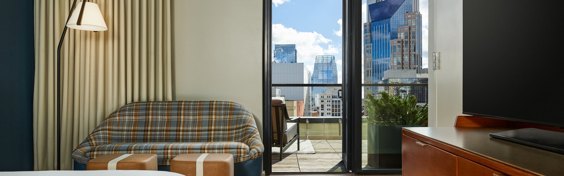 A penthouse suite at the Untitled Nashville with a king bed and seating area next to a terrace looking out on the Nashville skyline