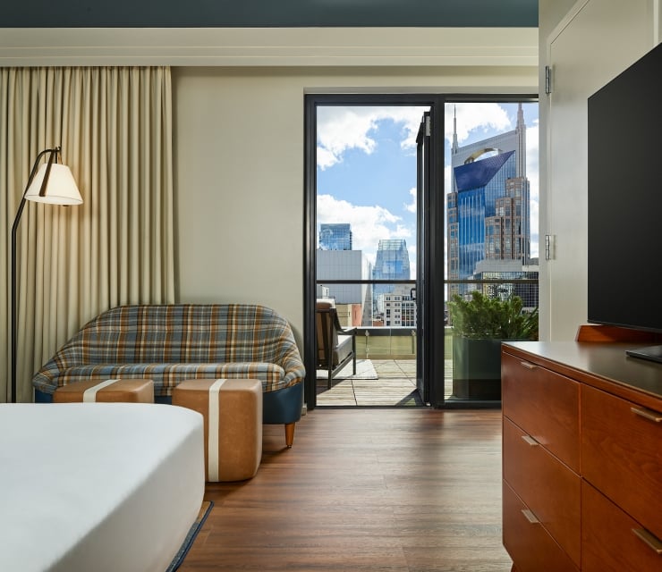 A penthouse suite at the Untitled Nashville with a king bed and seating area next to a terrace looking out on the Nashville skyline