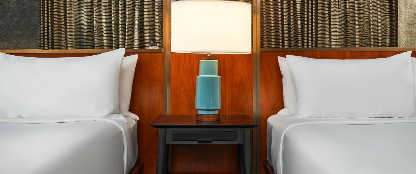 Two beds divided by a nightstand with a lamp on it at The Untitles Nashville Hotel