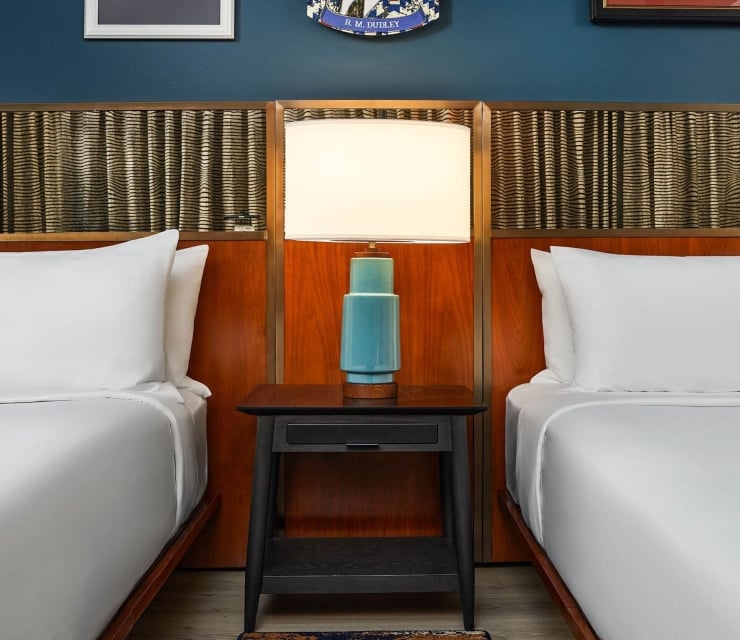 Two beds divided by a nightstand with a lamp on it at The Untitles Nashville Hotel