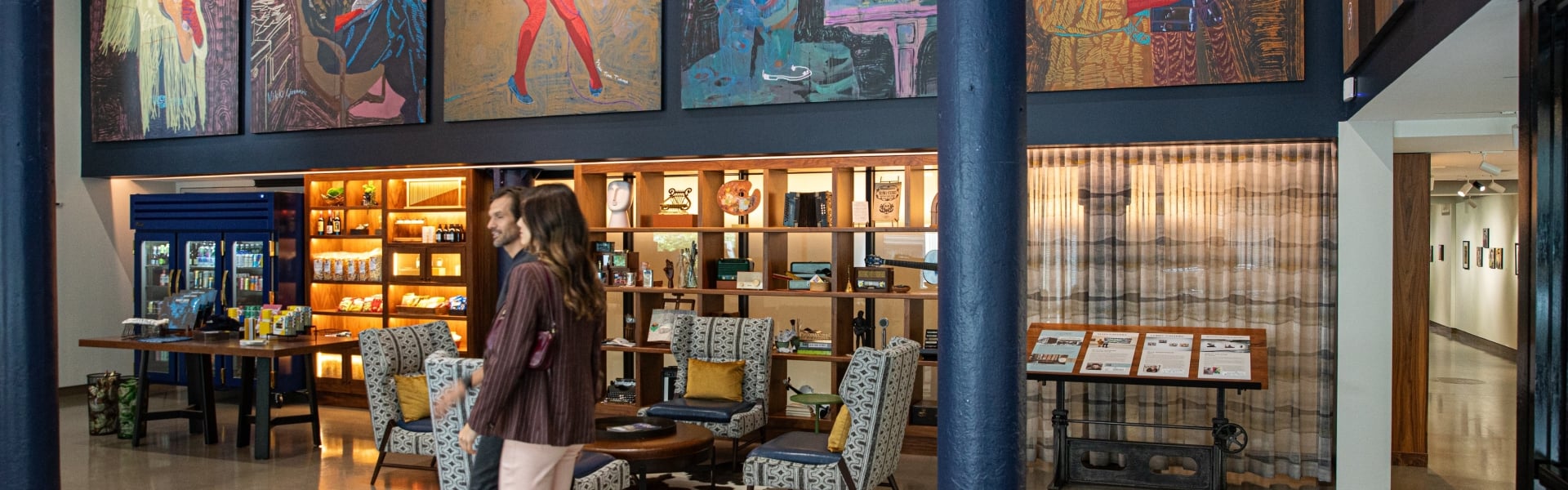 Two people walk through the lobby of tthe Untitled Nashville hotel, under an overhanging row of displayed artworks