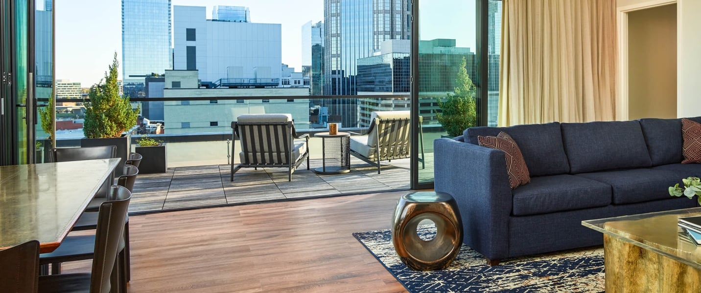 A modern living room with a navy sofa opens to an outdoor patio featuring two chairs and a city skyline view through large glass doors.