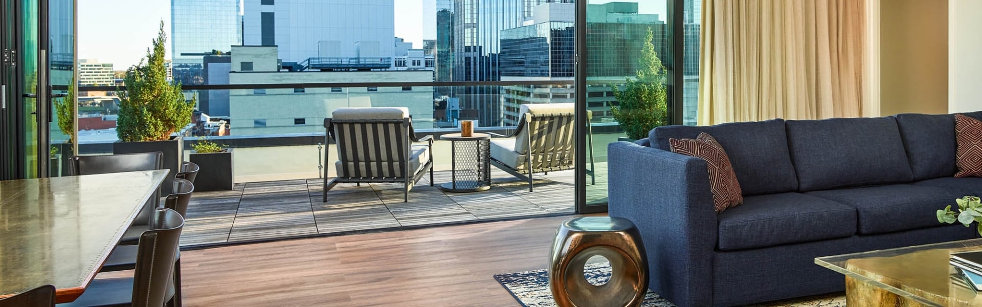 A modern living room with a navy sofa opens to an outdoor patio featuring two chairs and a city skyline view through large glass doors.