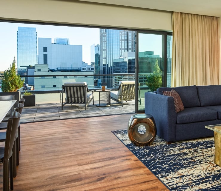 A modern living room with a navy sofa opens to an outdoor patio featuring two chairs and a city skyline view through large glass doors.
